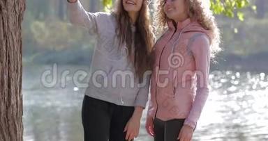 两个漂亮的小女孩在手机上拍照，靠近树户外日出，早秋公园
